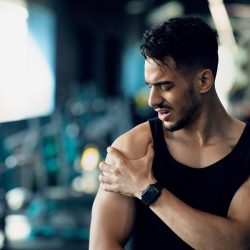 Sports Injury. Young Middle Eastern Man Suffering Shoulder Pain During Training At Gym, Arab Male Athlete Having Acute Muscle Ache, Touching Painful Area And Frowning, Closeup Shot With Copy Space
